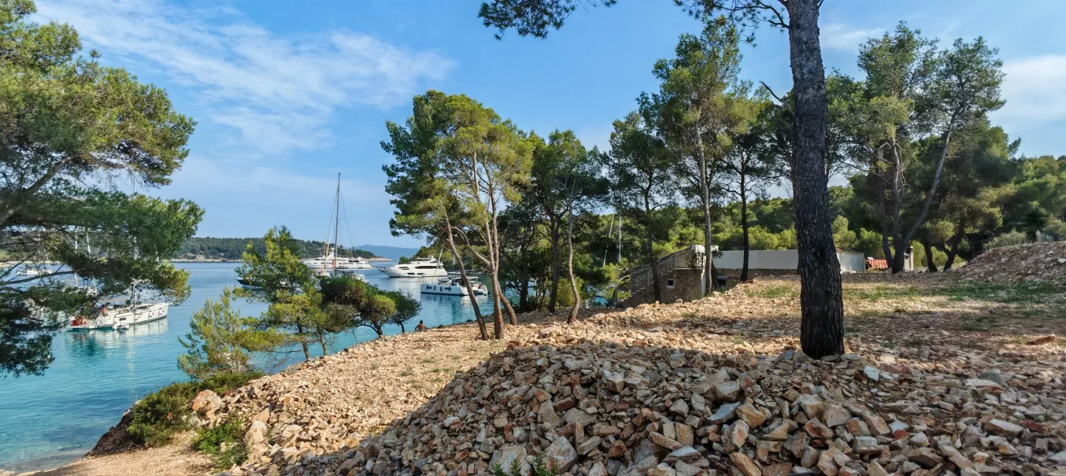 Pines, a gravel terrace and the bay below with sailing boats at anchor.