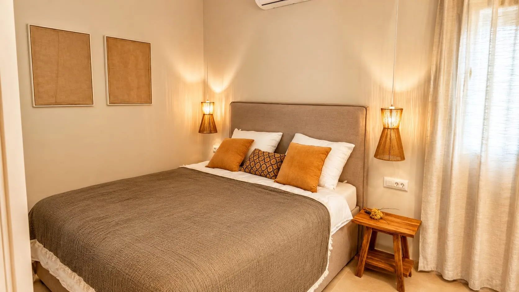 Bedroom with an upholstered headboard, two rattan wall lamps and linen curtains.
