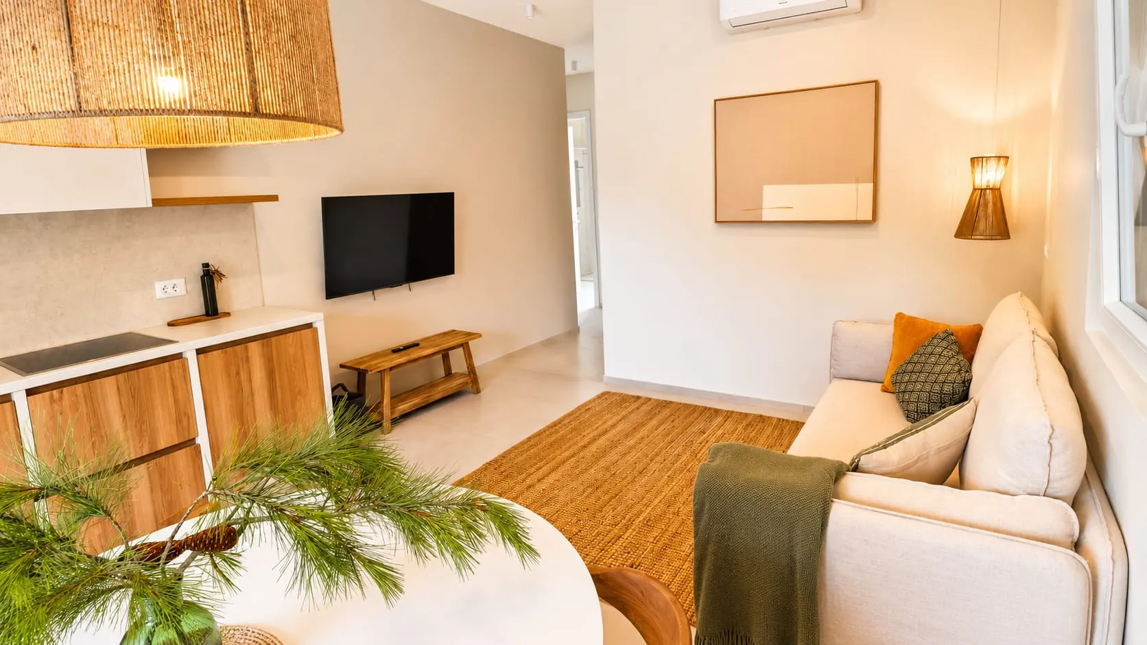 A finished apartment: linen sofa, oak kitchen, rattan lamp and a green throw.