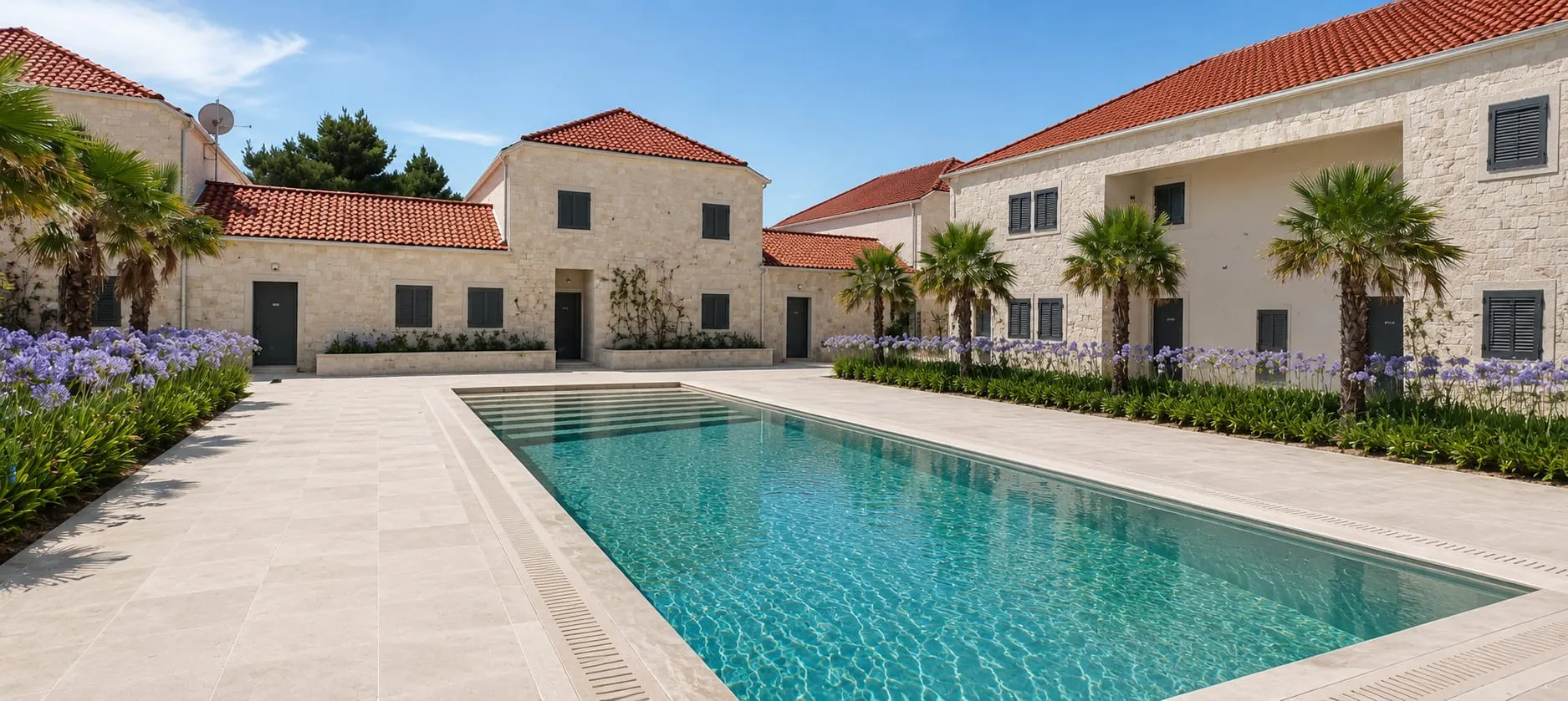 The pool courtyard of Pine Senses Resort: a long pool between two-storey stone houses with red roofs, palms and blue agapanthus.